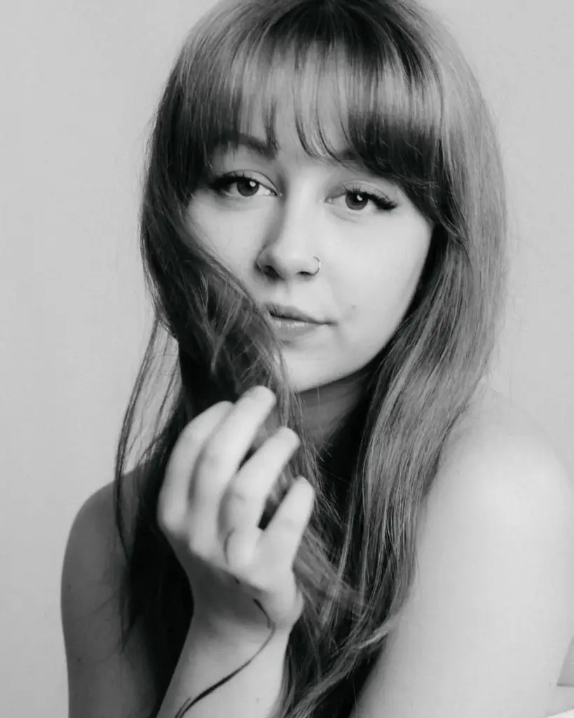 Schwarzweiß-Close-up einer Frau, Hand im Haar und ruhiger Blick in die Kamera