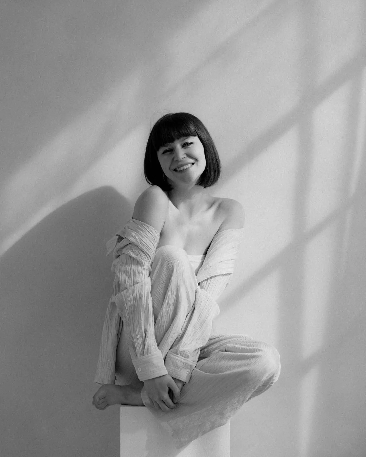 Schwarzweißporträt einer Frau, die auf einem Würfel sitzt und ruhig in die Kamera schaut