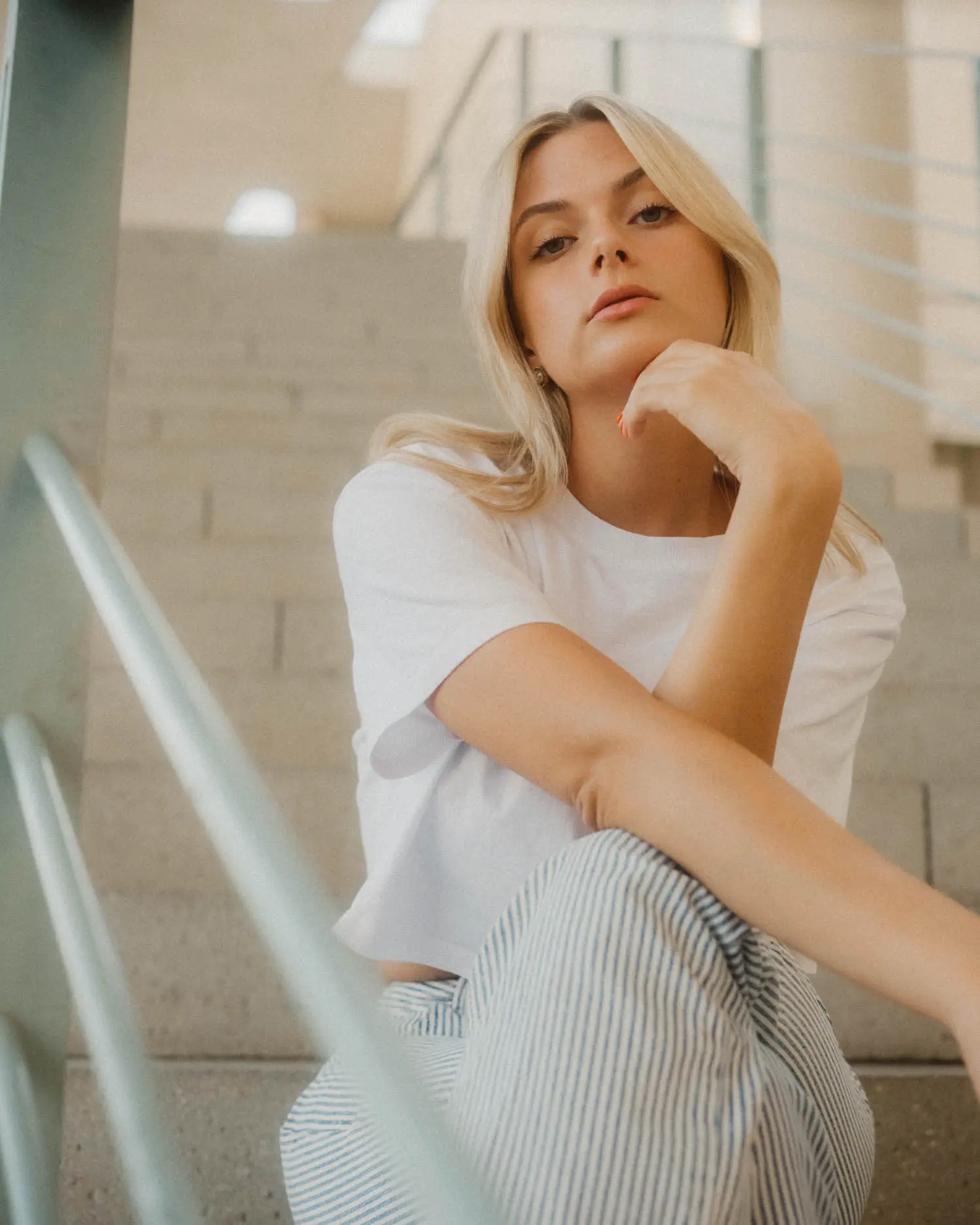 Frau sitzt auf einer Treppe und stützt das Kinn an, Blick gelassen und direkt