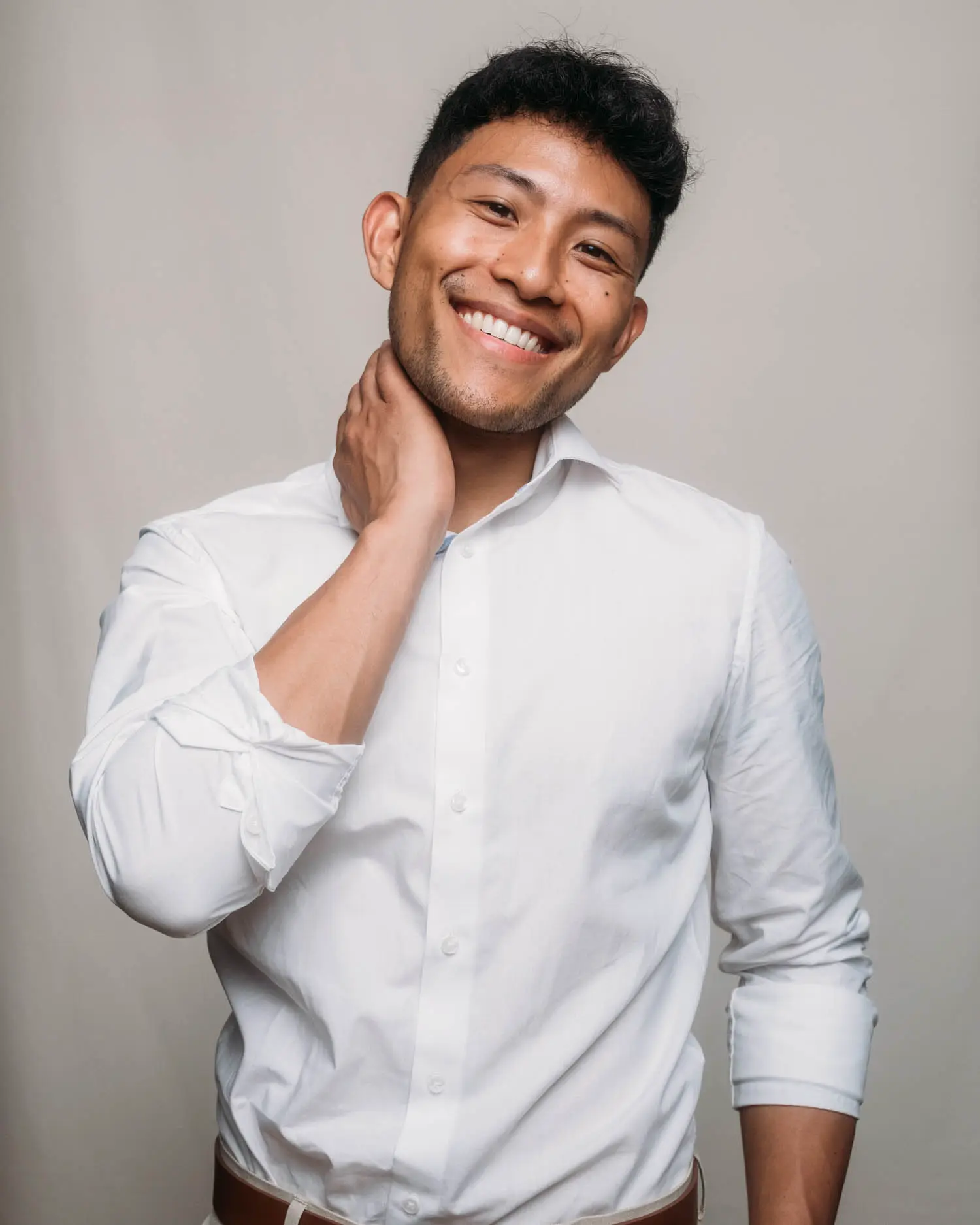 Studio-Portrait im weißen Hemd mit entspanntem Lächeln und Hand am Nacken