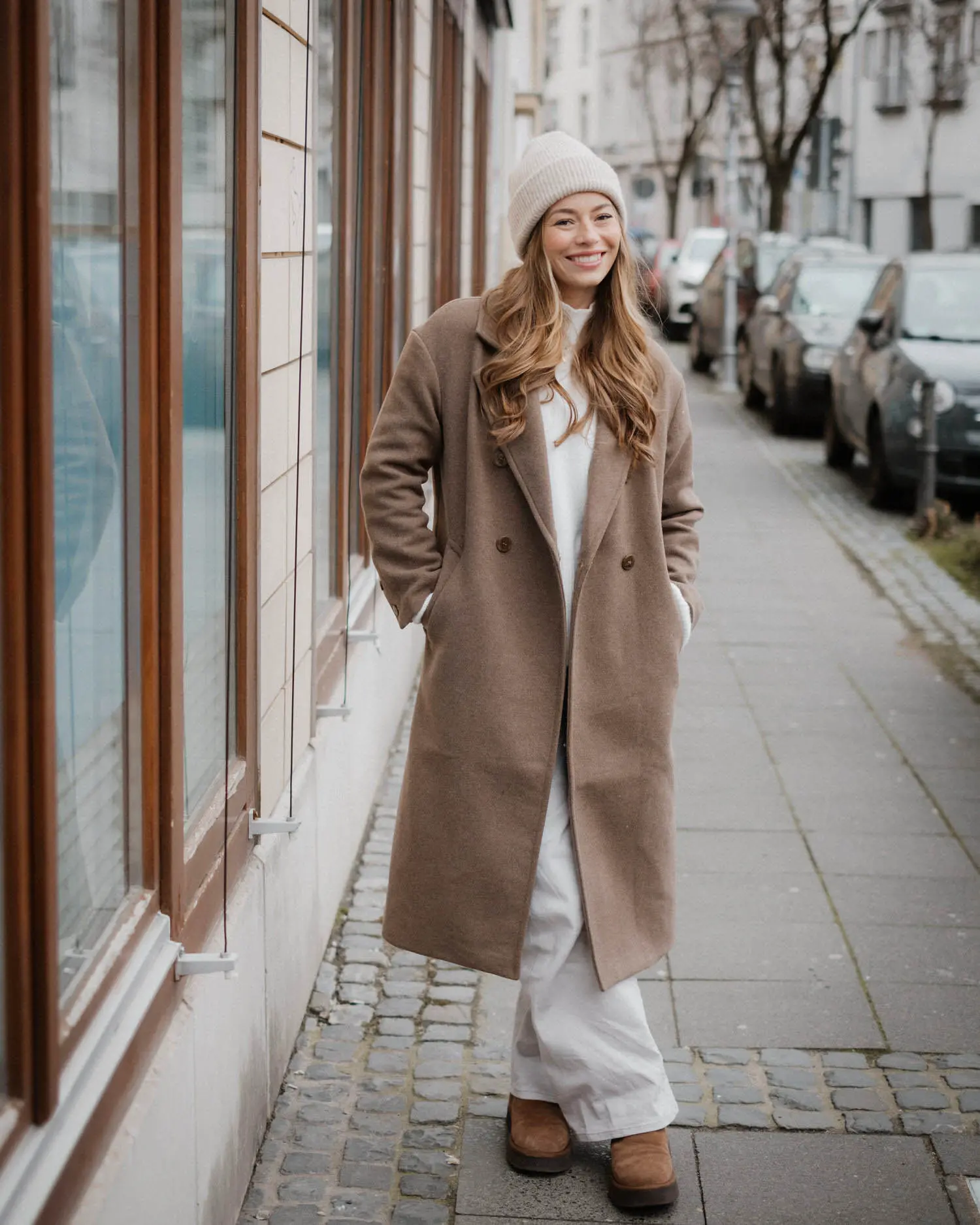 Frau im Mantel steht draußen im weichen Stadtlicht und blickt konzentriert zur Seite