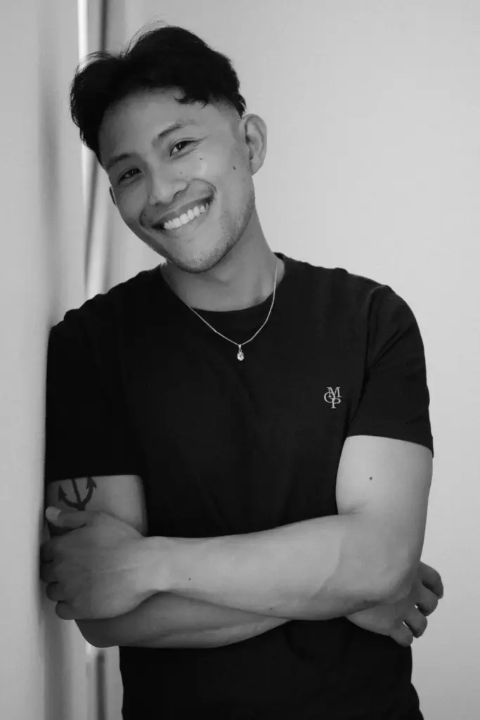 Schwarzweiß-Portrait eines Mannes mit verschränkten Armen und offenem Lächeln.