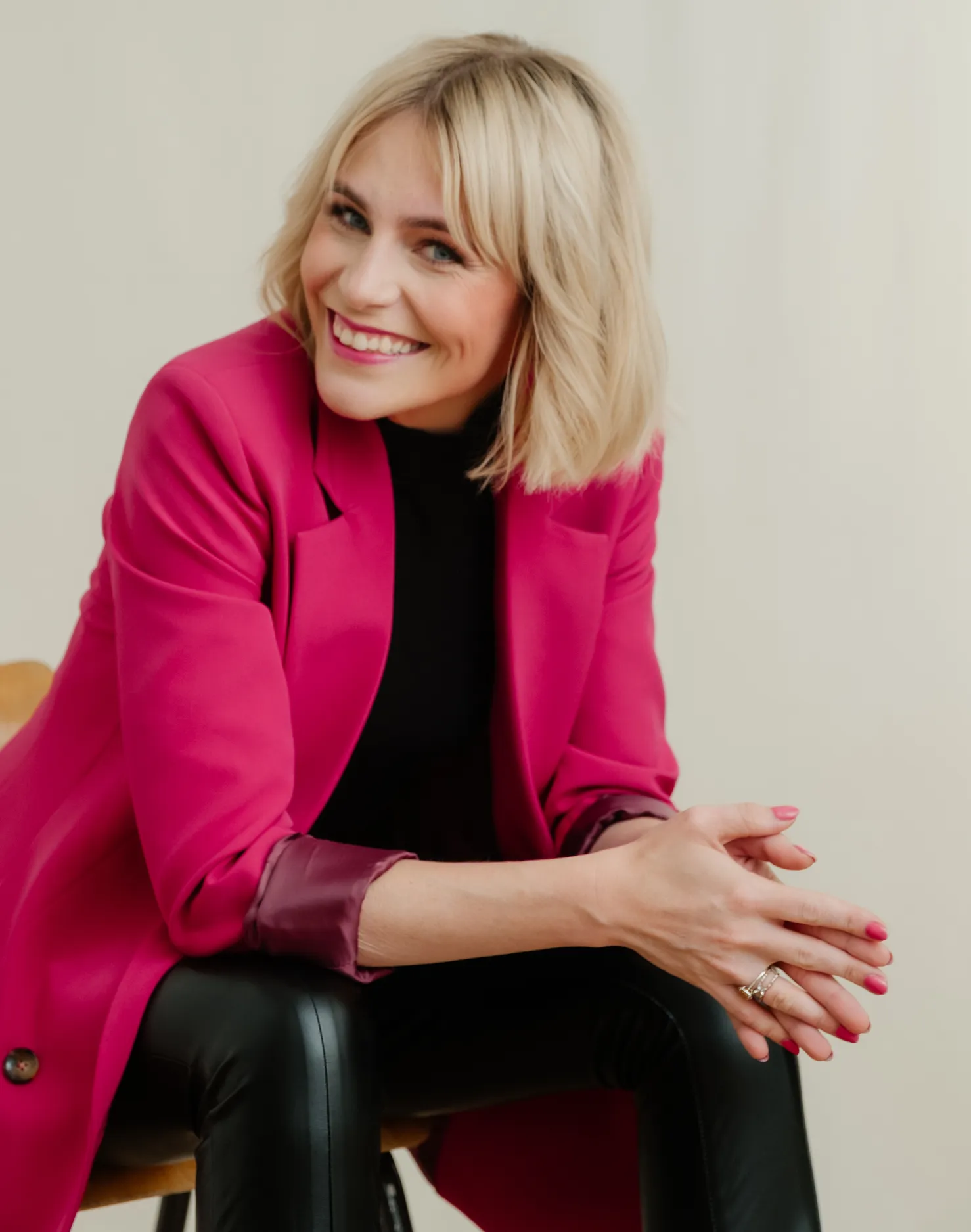 Frau im pinken Blazer sitzt im Studio und lächelt offen in die Kamera