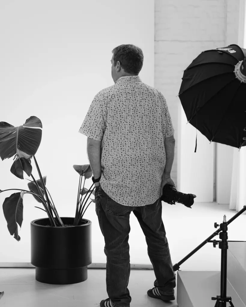 Schwarzweißszene im Fotostudio: Mann mit Kamera zwischen Pflanze und Softbox