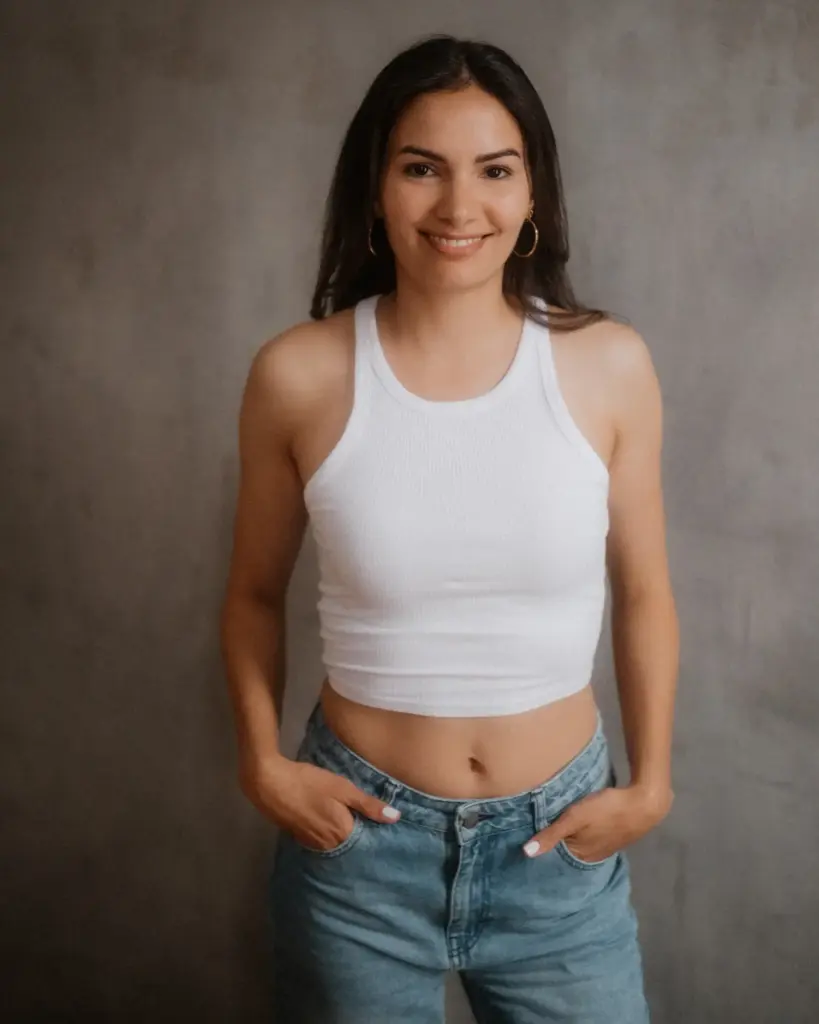 Studio-Portrait vor grauem Hintergrund, weiße Top-Kombination und freundliches Lächeln