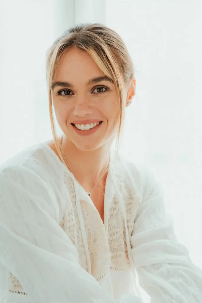 Natürliches Portrait im hellen Fensterlicht mit weißer Bluse und freundlichem Lächeln.