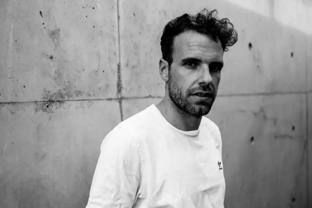 Schwarzweißaufnahme eines Mannes vor rauer Betonwand, Blick leicht seitlich