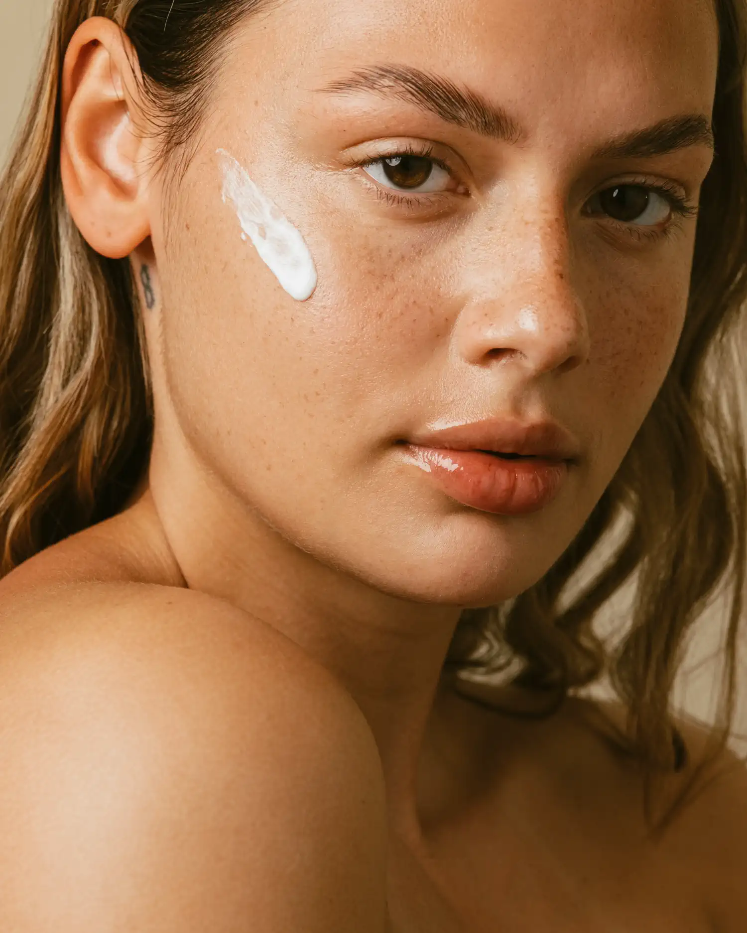 Beauty-Nahaufnahme eines Models mit Sommersprossen und einem Tupfer Creme auf der Wange