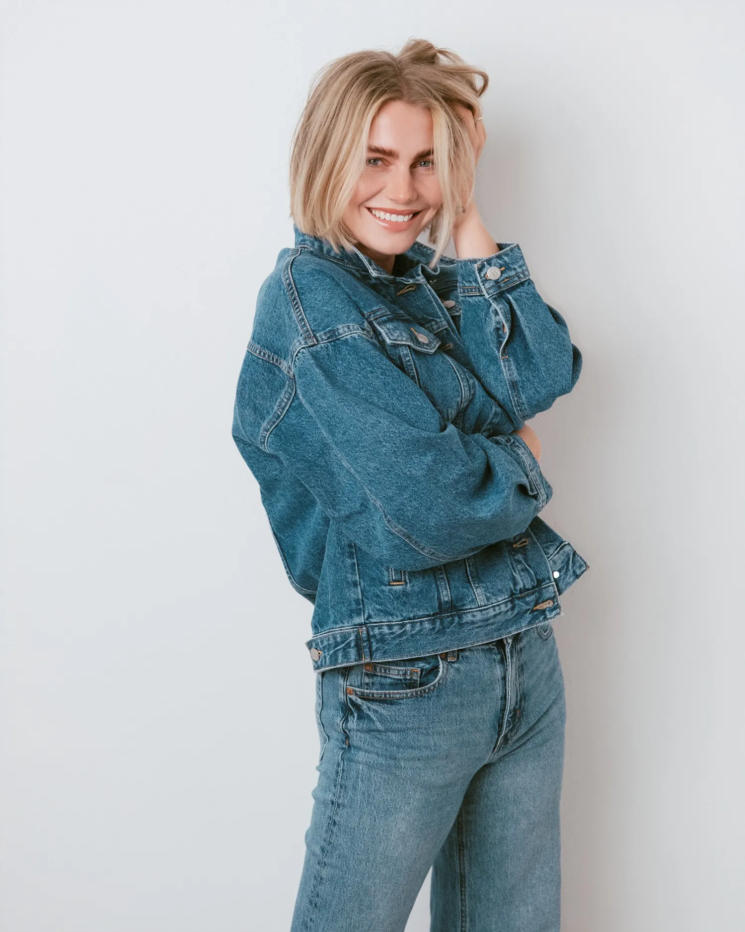 Lächelndes Model in Jeansjacke und Jeans vor hellem Hintergrund
