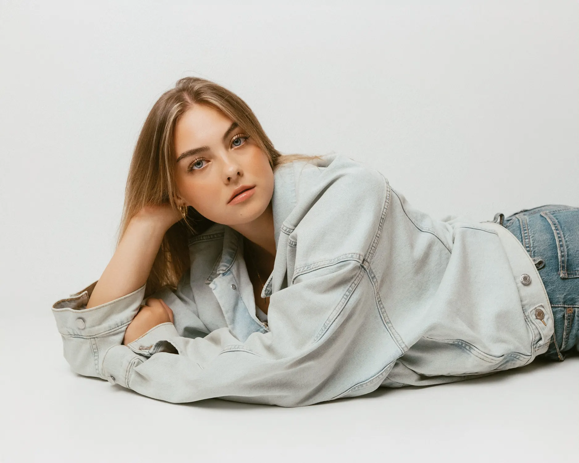 Model in heller Jeansjacke liegt vor weißem Studiohintergrund