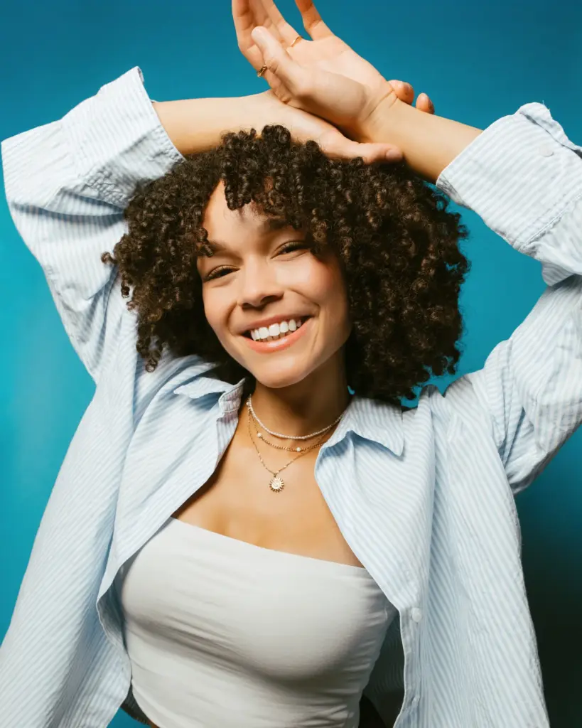Lächelndes Model mit Locken und hellem Hemd vor blauem Hintergrund