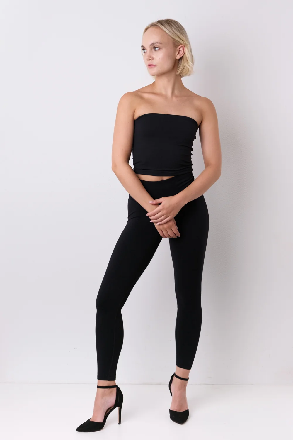 Ganzkörperaufnahme eines Models in schwarzem Outfit vor hellem Hintergrund