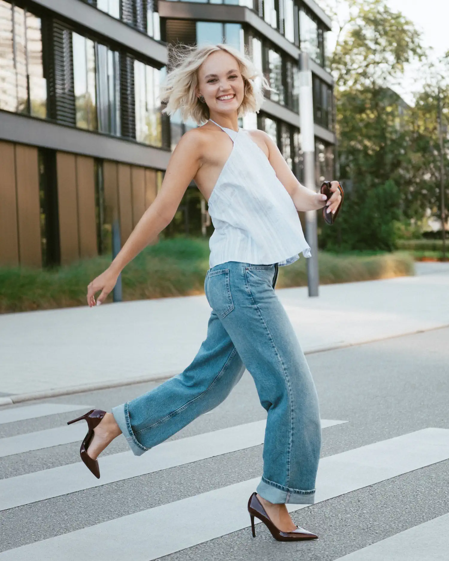 Lachendes Model in weißem Top und Jeans beim Überqueren eines Zebrastreifens