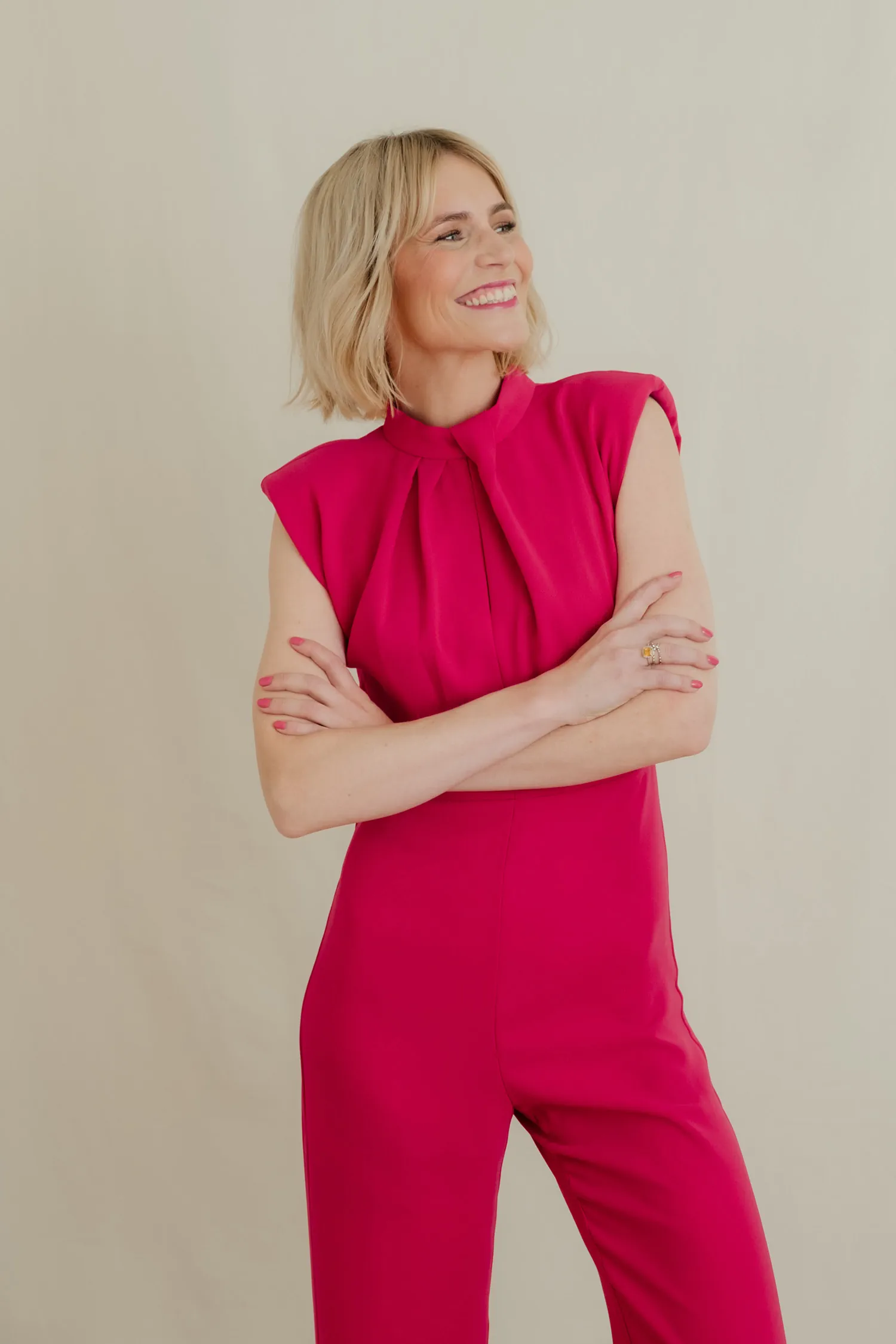 Julia Kleine im pinkfarbenen Jumpsuit mit verschränkten Armen, lächelnder Blick zur Seite
