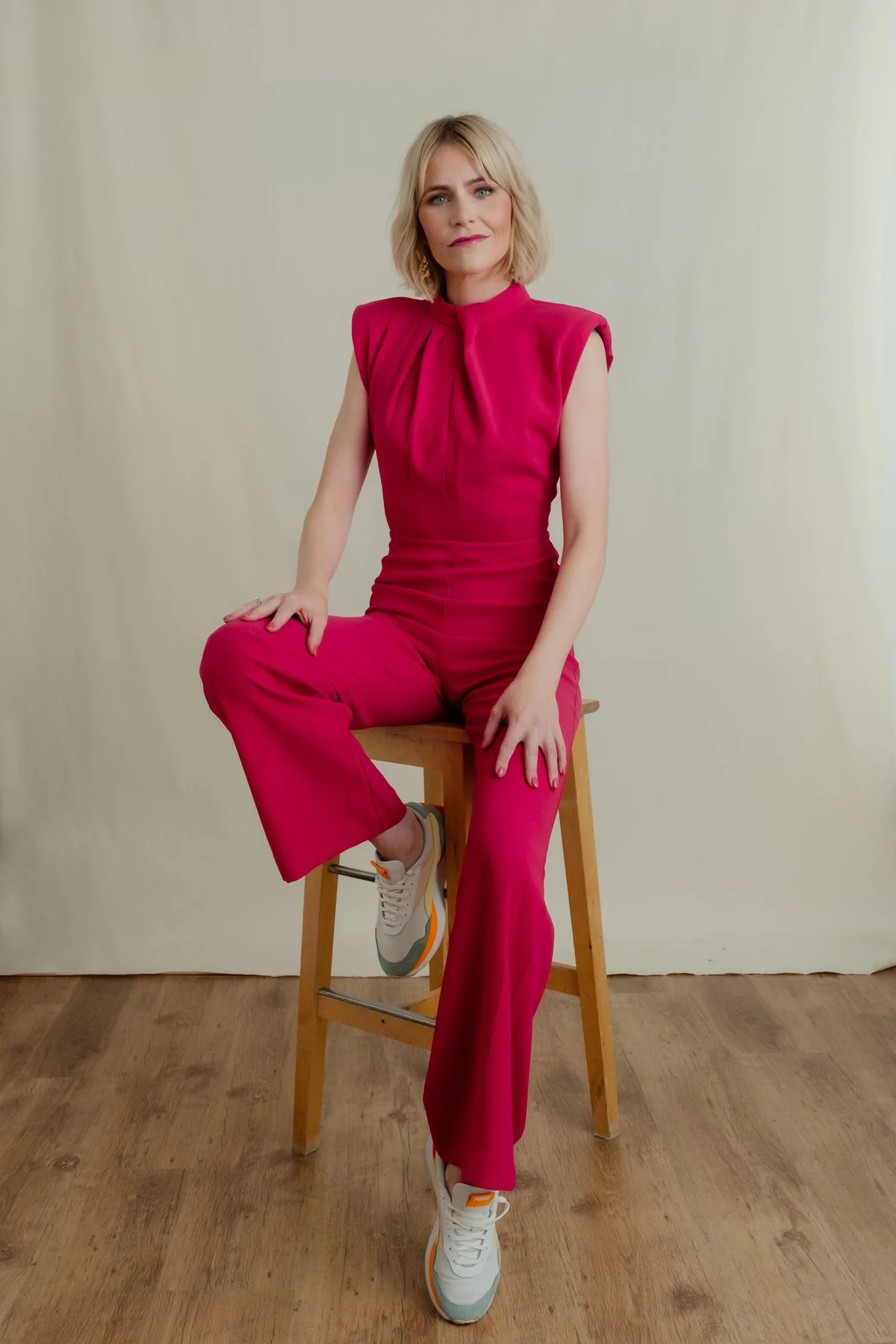 Personal-Branding-Portrait der Journalistin Julia Kleine im pinkfarbenen Jumpsuit auf einem Holzhocker im Studio