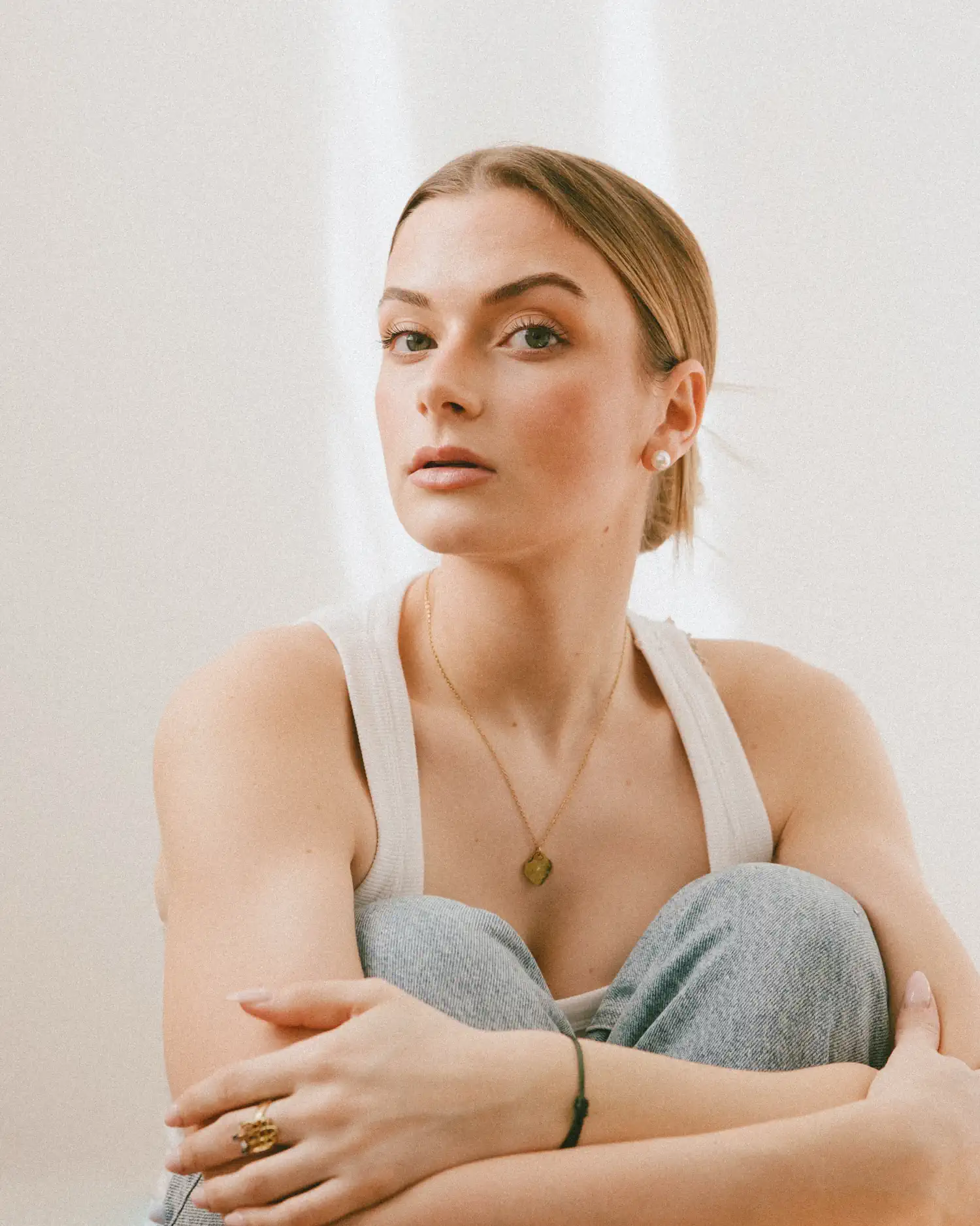 Portrait eines Models im weißen Top, mit angezogenen Knien und Blick in die Kamera