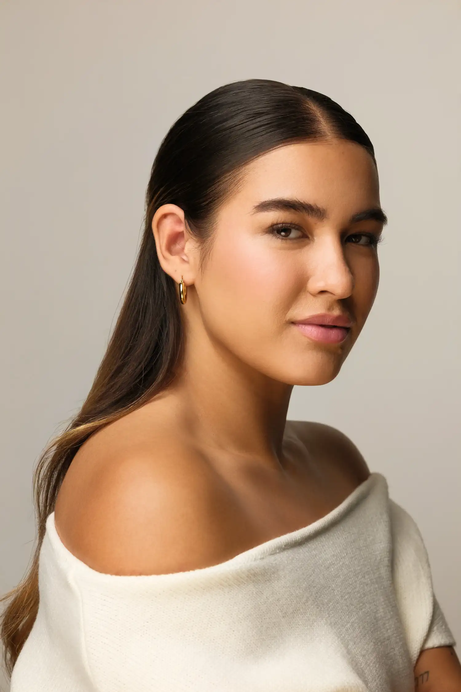Portrait eines Models mit zurückgenommenem Haar und weißem schulterfreiem Oberteil vor beigem Hintergrund