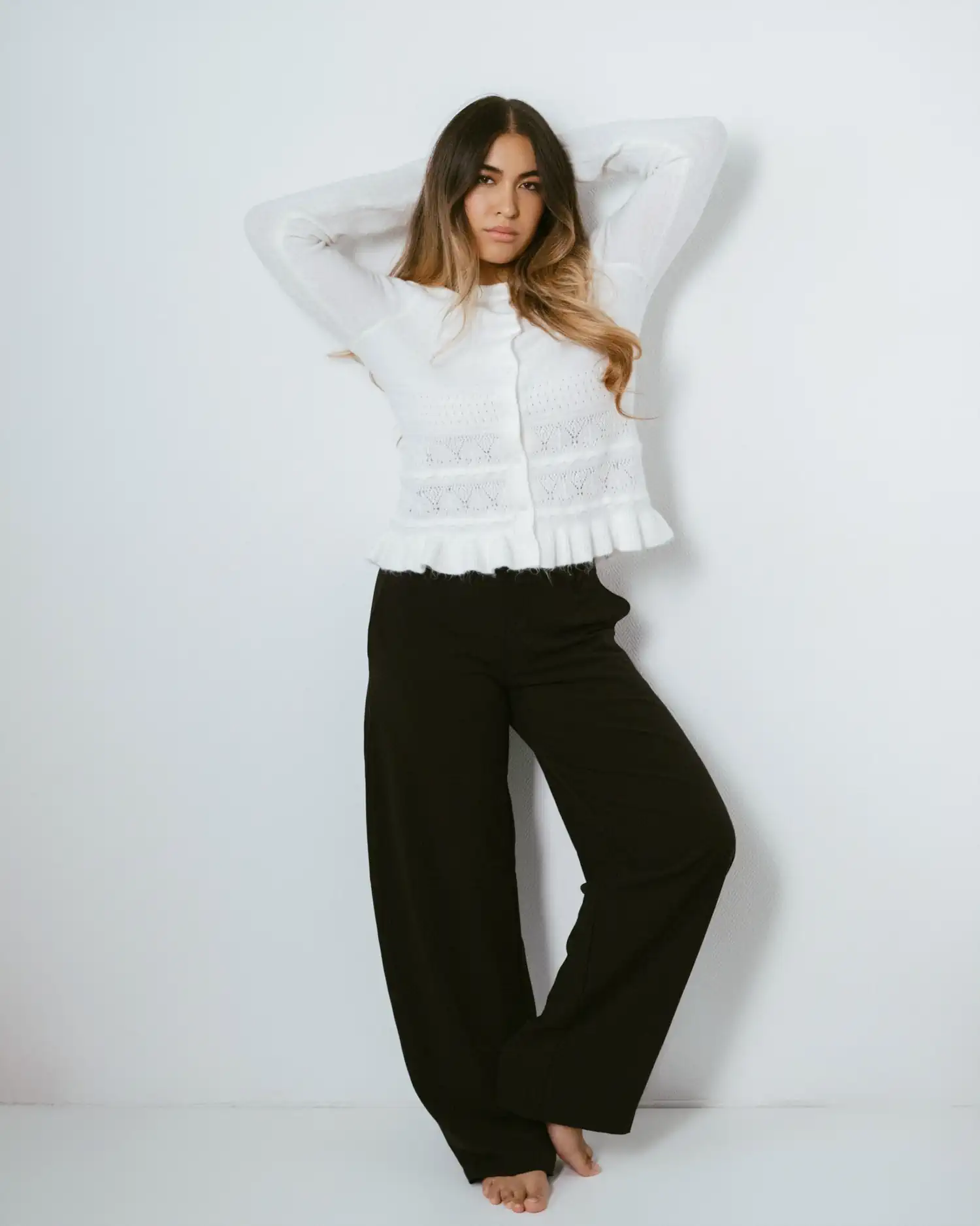 Ganzkörperaufnahme eines Models in weißer Bluse und schwarzer Hose, barfuß mit den Händen hinter dem Kopf